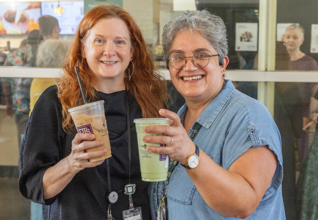 Two women smiling and holding iced coffee 